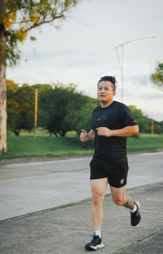 A man jogs along a suburban street in athletic wear during the day, surrounded by greenery.