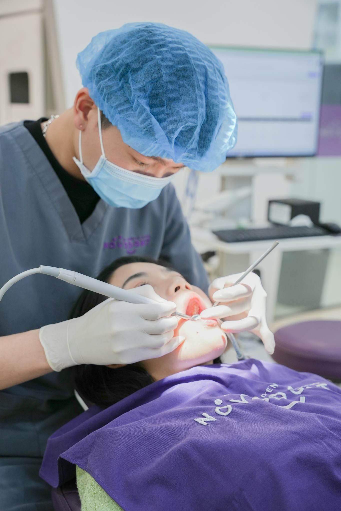 Dentist wearing surgical mask and cap, treating a patient in a dental clinic.