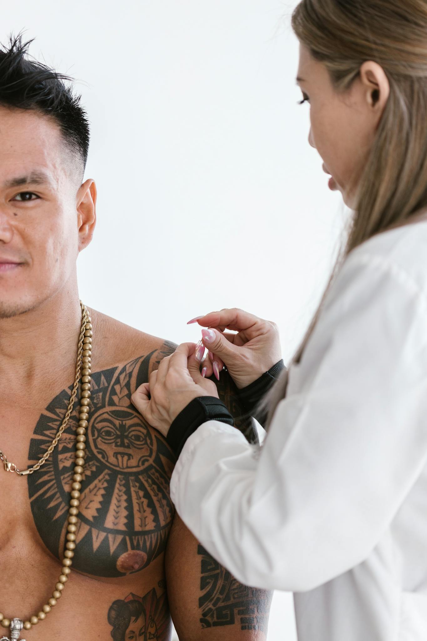 Healthcare professional giving an injection to a man with tattoos and beads visible.