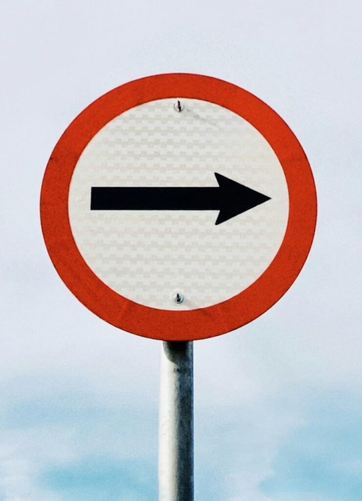 Minimalist shot of a directional street sign on a pole against a clear blue sky.