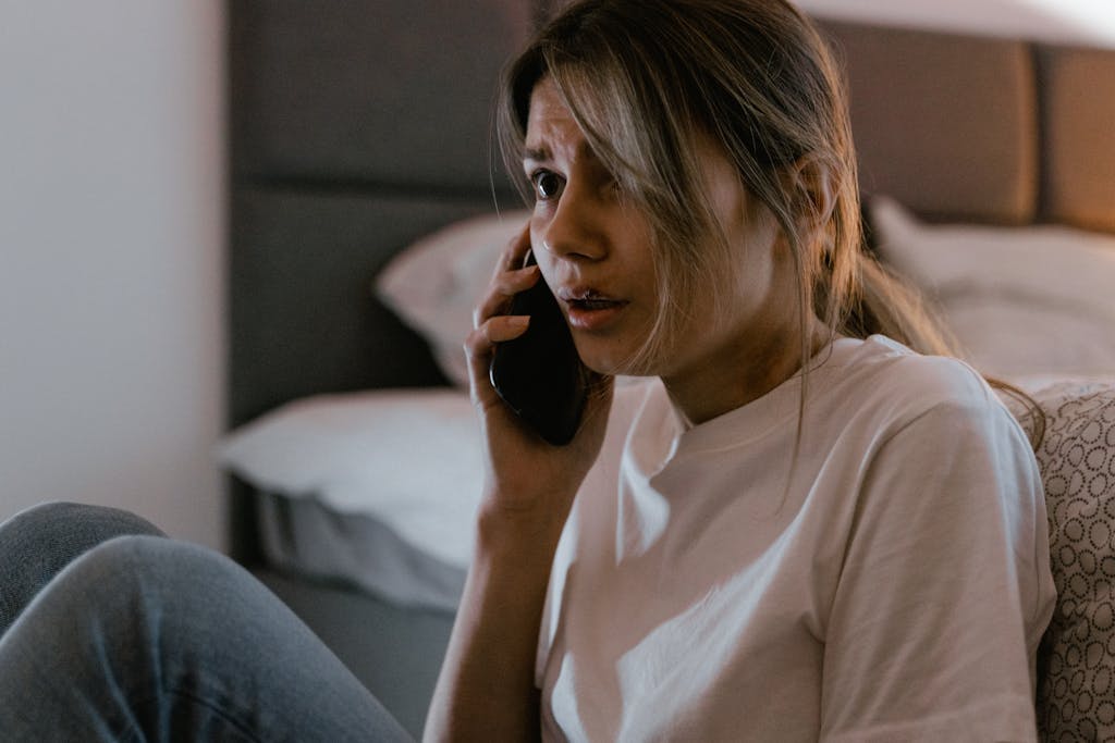 A worried woman in a white shirt making a distressing phone call for help.